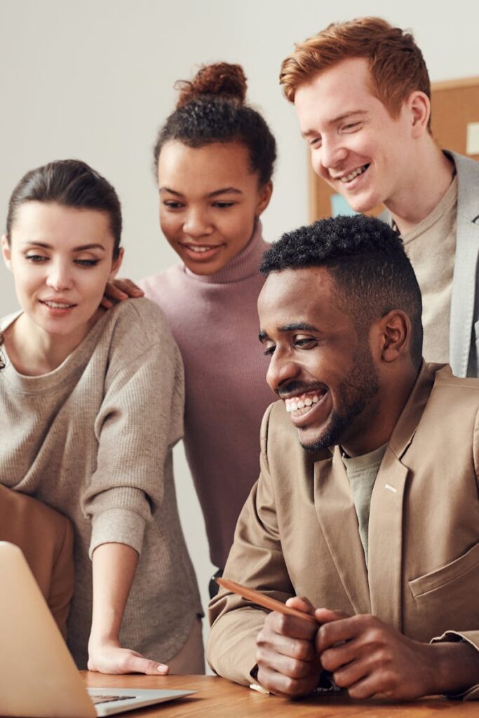 A group of diverse young professionals happily collaborating around a laptop indoors.